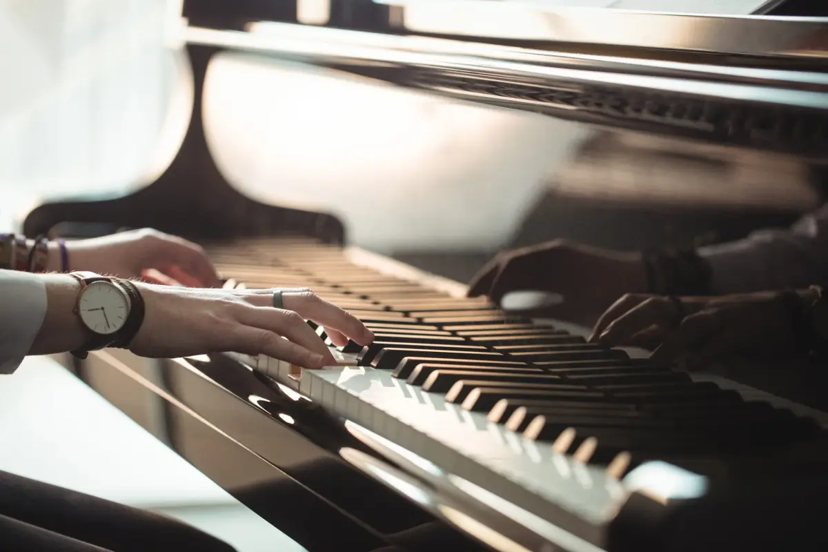Ręce osoby grającej na fortepianie. Ręce są położone na klawiszach, zegarek na nadgarstku wskazuje elegancję.