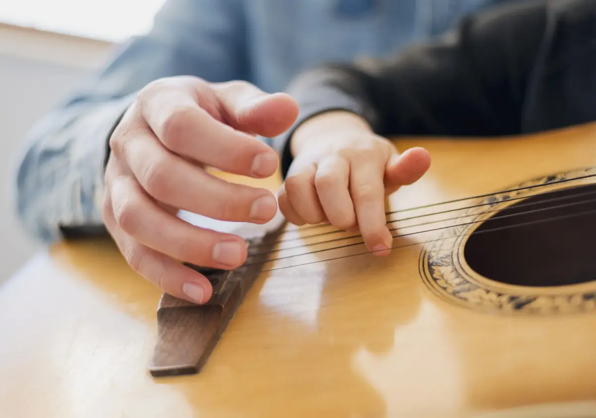 Zbliżenie na ręce osoby grającej na akustycznej gitarze na drewnianym stole.