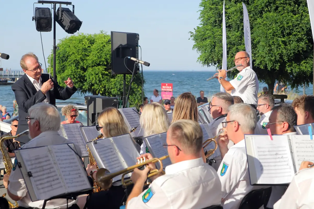 Orkiestra na żywo wykonująca muzykę na zewnątrz z widokiem na morze w tle.