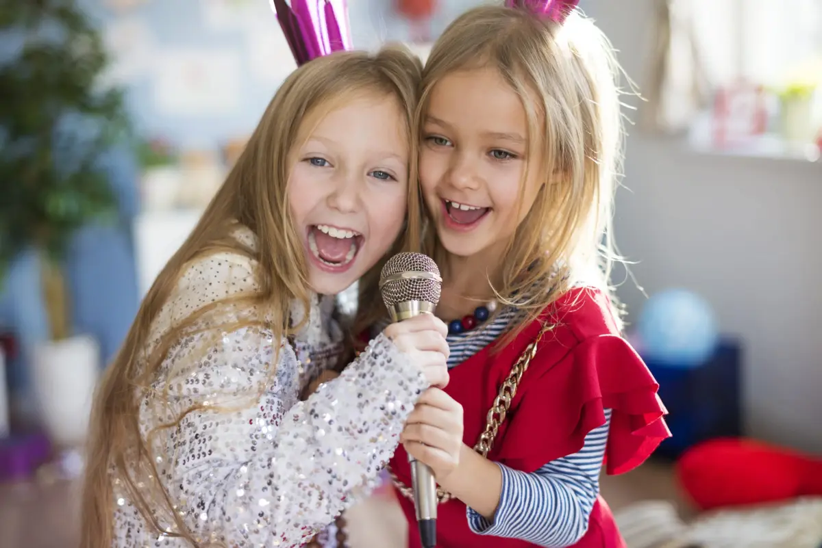 Dwie młode dziewczynki śmiejące się i śpiewające do mikrofonu razem na przyjęciu.
